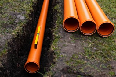 Turuncu PVC drenaj borularını yere seriyor.