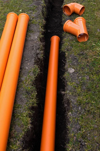Laying down orange PVC drainage pipes into the ground