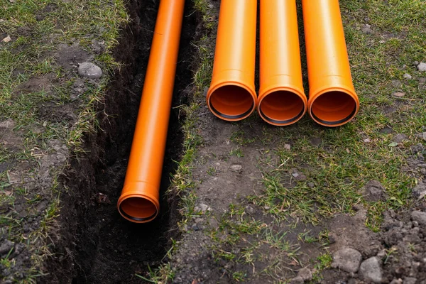 Laying down orange PVC drainage pipes into the ground