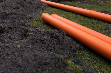 Turuncu PVC drenaj borularını yere seriyor.