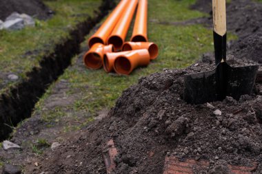 Turuncu PVC drenaj borularını yere seriyor.