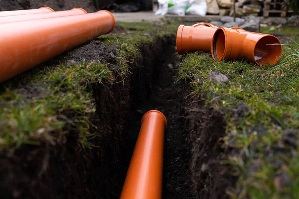 Laying down orange PVC drainage pipes into the ground