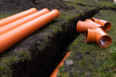 Turuncu PVC drenaj borularını yere seriyor.