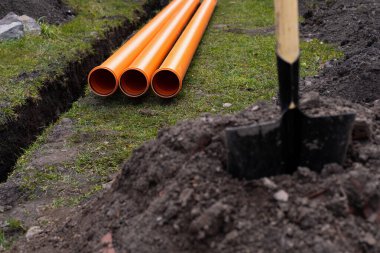 Turuncu PVC drenaj borularını yere seriyor.