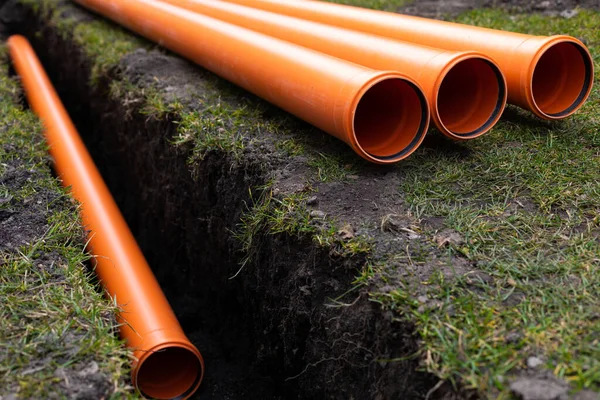 Laying down orange PVC drainage pipes into the ground