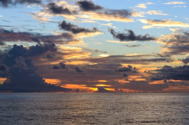 Gün batımını açık okyanusta, bulutların arka planına karşı, güneş ışınları yarıp geçerken.