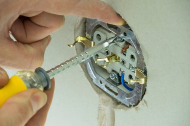 Elektrikçi prizleri elektrik kablolarına bağlar. Kabloyu fişe takın. Adamın biri duvara elektrik prizi takıyor. Tornavidayı güç prizinin yanında tutan teknisyenin yakınına..