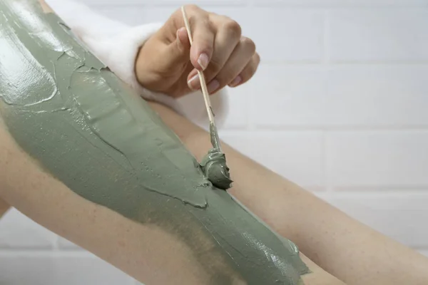 SPA, nemlendirici, tedavi. Bir kadın kilden bir maskeyi bacaklarının derisine bir spatulayla sürer. Tüyleri alındıktan sonra tahriş, tıraş. Evde cilt bakımı, vücut. Deri dökülmesi, soyulma. Çilek bacakları.
