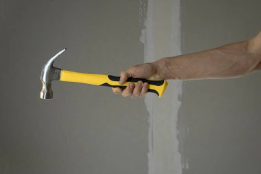 Bir adam boyalı bir duvara karşı sarı bir çekiç tutuyor. Ev tamiri yap. Diy. Çekiçli marangoz elleri. Evi tamir etmek için aletler. Evini geliştir. Tamir için bir işçi tutmak. İnşaat işçisi