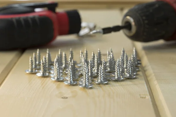 Electric drill with drill bits, screws on wooden background. Bunch of screws on wood planks. Assorted tools. Handyman professional DIY project workplace tabletop. Cordless drill and screws.