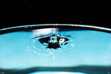 Yuvarlak dalgalı temiz su damlası. Yakından su sıçratıyor. Su sıçrıyor ve düşüyor. Düşen su damlalarından bir damla. Mavi arka planda su damlası. Su sıçratan mavi su yüzeyi.