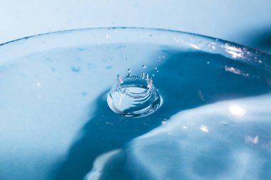 Su, taç şeklinde sıçrar ve düşer. Düşen su damlalarından bir damla. Mavi arka planda su damlası. Su sıçratan mavi su yüzeyi. Yuvarlak dalgalı temiz su damlası. Yakından su sıçratır