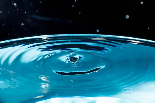 Water drop on blue background. Blue water surface with splash. Clear Waterdrop with circular waves. Splashes closeup. Water splash and falling drop. Splash of the falling drops of water.