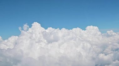 Bulutların üstünde mavi gökyüzü olan bir uçak penceresinden 4K