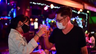 4K Asyalı çift bira kızartıyorlar ve Khao San yolunda içmek için cerrahi maske takıyorlar.