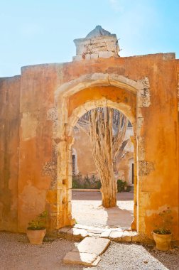 Arkadi Manastırı avlusunda kapısı olan ortaçağ duvarı. Duvarın arkasında, Girit, Yunanistan 'da ölü bir ağaç var.