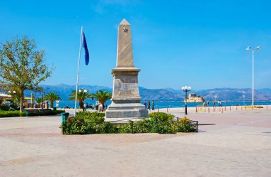 Philellinon Meydanı 'ndaki Fransız filozoflarına adanmış taş dikilitaş, Argolik Körfezi ve Bourtzi Şatosu manzaralı, Nafplio, Yunanistan