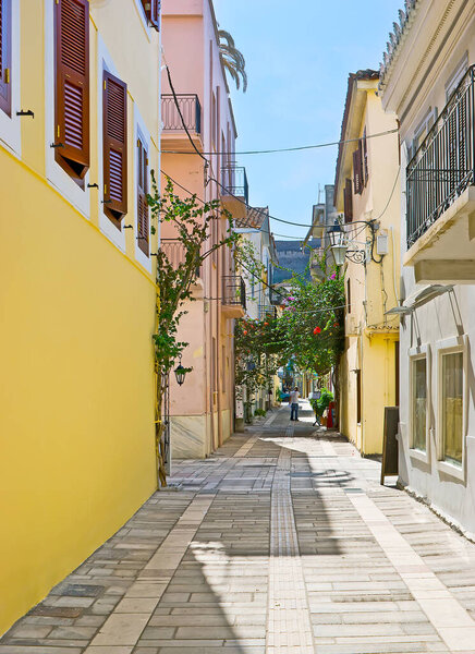 The narrow street with colored houses and blooming shrubs, located in port neighborhood of Nafplio, Greece