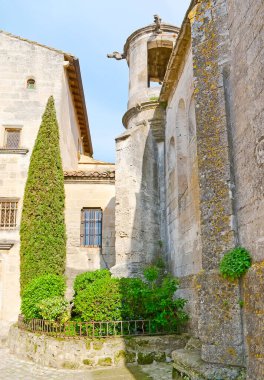 Köşesi ve St. Vincent Kilisesi kulesi olan ortaçağ taş kasabası Les Baux-de-Provence yeşil bitkiler ve thuja ağacı olan küçük çiçek yatağı, Fransa