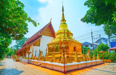 Wat Phra Singh 'in altın çadırı, küçük stupalarla süslenmiş, bahçenin yemyeşil yeşiliyle çevrili, Chiang Rai, Tayland