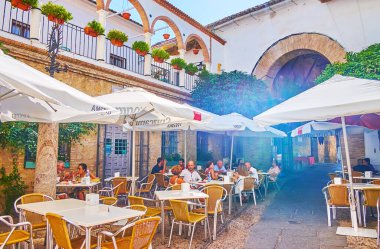CORDOBA, SPAIN - 30 SEP 2019: 30 Sep 'te Cordoba' da Ay Kapısı olan açık hava restoranının masaları ve güneş gözlükleriyle dar Calleja de la Luna caddesi