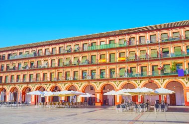 Corredera Meydanı 'ndaki parlak turuncu detaylar ve atari salonlarıyla süslenmiş uzun manzaralı bina, Cordoba, İspanya