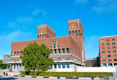 The scenic view of Oslo City Hall from the Radhusplassen with a view of the giant clock atop the tower and the sculpture of St Hallvard on the brick wall, Oslo, Norway