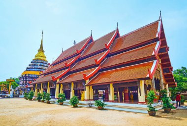 Arka planda Lampang Luang Tapınağı, Lampang, Tayland 'daki Viharn Luang' ın sütunları, gaçalı çatısı ve Chedi of Wat Phra binası var.