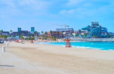 The sand coast of La Mer public beach with a view of the water park, Dubai, UAE