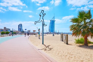 The jogging alley along the sand Jumeirah beach with a modern jogger installation and Burj al Arab in the background, Dubai, UAE
