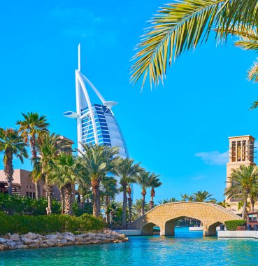 Souk Madinat Jumeirah pazarının kanalı boyunca uzanan uzun yeşil palmiyeler, fütürist Burj al Arab arka planda, Dubai, BAE