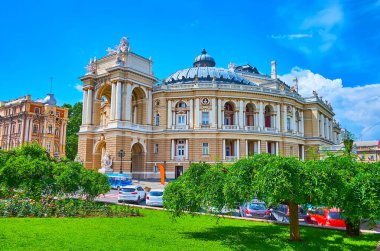 Tiyatro Meydanı 'nda (Teatralna Meydanı) yemyeşil ağaçlar ve arka planda Opera ve Bale Tiyatrosu' nun etkileyici tarihi binası, Odessa, Ukrayna