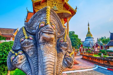 The vintage five-headed Naga serpent statue against the garden and Chedi of Wat Buppharam, Chiang Mai, Thailand