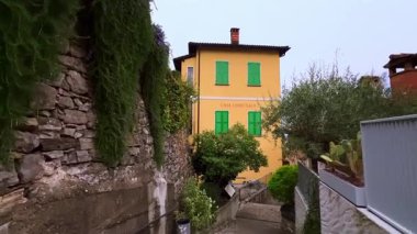 Renkli evleri, yeşil bitkileri ve çiçekli biberiye çalıları olan eski dar sokaklar taş duvarda asılı, Gandria, Ticino, İsviçre