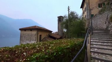 Tepedeki uzun merdivenler ortaçağ San Vigilio Kilisesi ve ağaçların ve çalıların arkasındaki eski evlerin çatıları, Gandria, Ticino, İsviçre