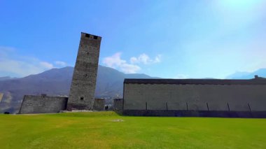 Güneşli bir günde Castelgrande Panoraması 'nda yeşil kort, taş kuleler, surlar ve arka planda Lugano Prealpleri, Bellinzona, İsviçre