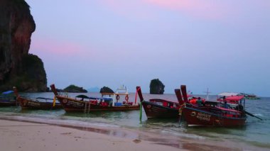 AO NANG, THAILAND - 26 Nisan 2019: 26 Nisan 'da Ao Nang yarımadasında, gün batımında Phra Nang sahilinde dalgalar üzerinde sallanan eski model botlar