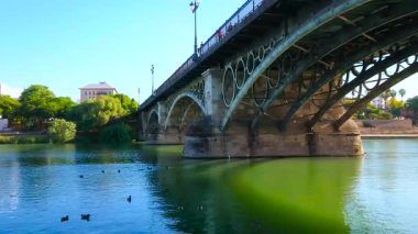 Seville, İspanya - 2 Ekim 2019: Guadalquivir nehri üzerindeki kemerli Isabel Köprüsü manzarası ve Triana bölgesinin karşı kıyısındaki yemyeşil arazi, 2 Ekim 'de Seville' de