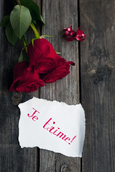 Trois roses rouges sur table rustique avec des mots écrits à la main je t'aime — Photo