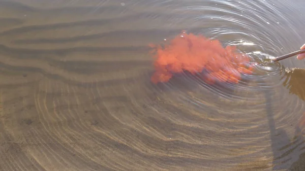 Het meisje laat een borstel met rode verf in de rivier zakken. Het water wordt rood. Hand met scheurplan. — Stockfoto