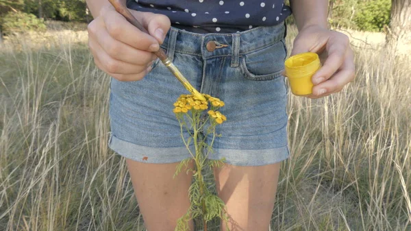 Uma jovem pinta uma flor amarela. Uma mulher pinta uma planta com um pincel. — Fotografia de Stock