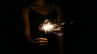 Bir kadın elinde Bengal ateşi tutuyor. Maytap karanlıkta parlar. Maytaplı bir el.