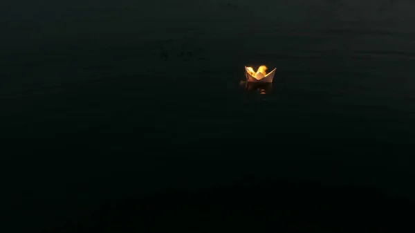 Una barca di carta galleggia lungo il fiume e brucia nel cuore della notte. Origami di carta. — Foto Stock