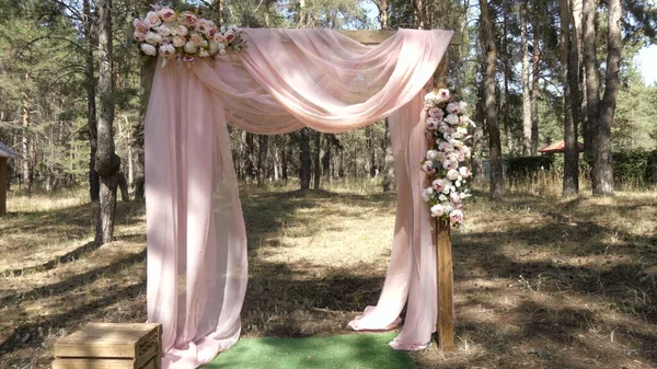 Ein Hochzeitsbogen steht in einem Kiefernwald. Das Hochzeitsdekor ist mit Blumen dekoriert. — Stockfoto