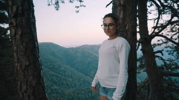 Gözlüklü genç bir kız uçurumda duruyor ve yeşil dağlara bakıyor. Arkadan bak. Dağları aşın. — Stok fotoğraf