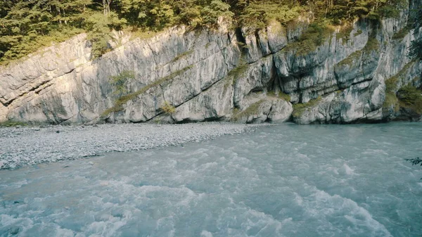 A turquoise river flows along the cliff. The mountain river flows rapidly.