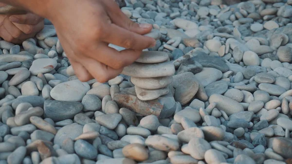 A fiatalok a parton játszanak, és köveket raknak egymásra. Kavicsos tornyot építenek közelről.. — Stock Fotó