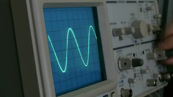 Diagramma di ampiezza sull'oscilloscopio. Un uomo preme i pulsanti sul dispositivo. La linea geometrica cambia forma — Foto Stock
