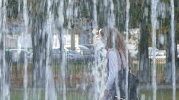 Молода жінка йде біля фонтану. Вид через фонтан — стокове фото