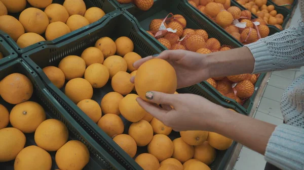 La jeune femme choisit des oranges au marché. Filles mains gros plan. — Photo